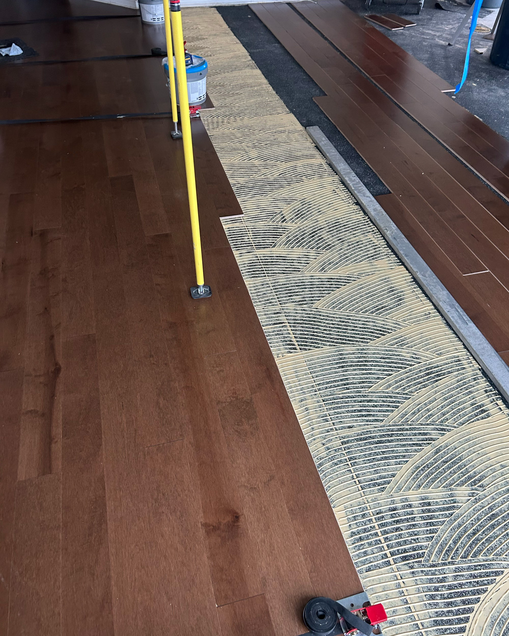 Dark hardwood glue-down installation showing carefully combed adhesive
