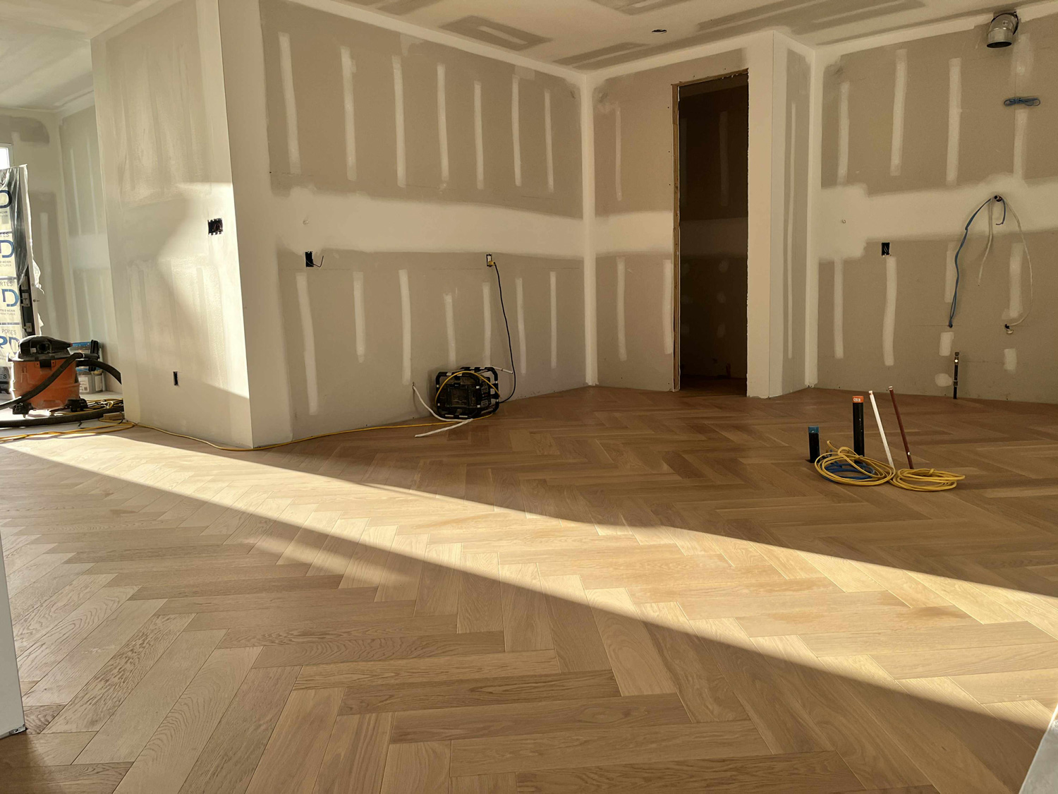 Sunlit natural oak herringbone flooring installed across a large open room