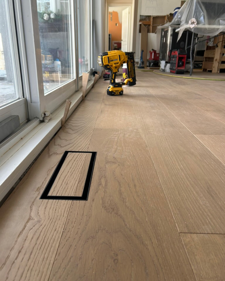 Wide plank light oak hardwood flooring with a flush wood floor vent during an Ottawa installation